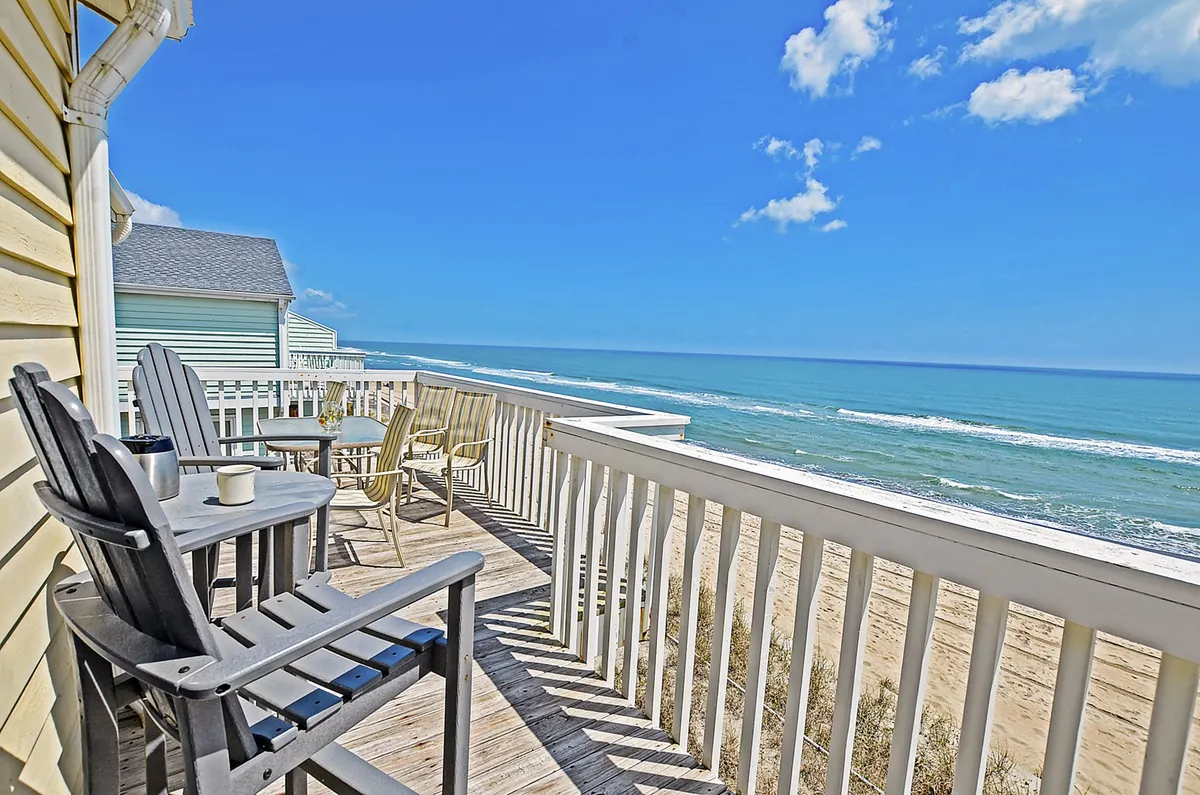 The image showcases a serene private deck overlooking the sparkling Atlantic Ocean, with comfortable deck chairs positioned to enjoy panoramic sunrise views. A sturdy wooden railing frames the space, inviting guests to relax, soak up the sun, sip their morning coffee, or unwind under a tranquil evening sky, all with the soothing sound of waves in the background.