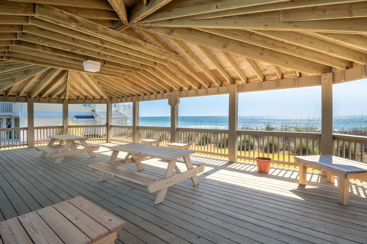 An open beachfront pavilion with wooden picnic tables, offering panoramic ocean views and a breezy spot for gatherings. The pavilion sits close to the shoreline, inviting shared meals, sunset watching, or simply enjoying the sounds of the surf.