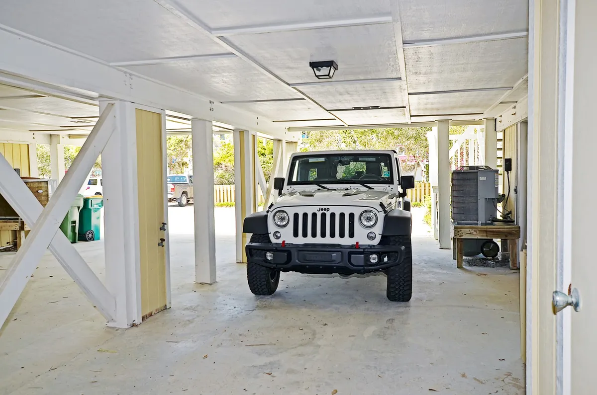 A Jeep Wrangler is parked under the house in an open, shaded space supported by sturdy beams. This practical area is used for storing outdoor gear and prepping for adventures, with easy access to and from the property.