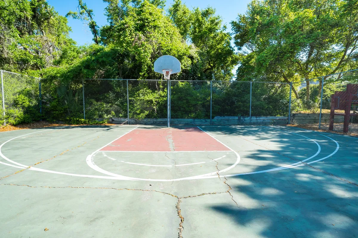 An exterior shot of a basketball court surrounded by trees, showcasing a hoop, court markings, and an inviting open space for active recreation. The setting is energetic and outdoorsy, suitable for guests of all ages.