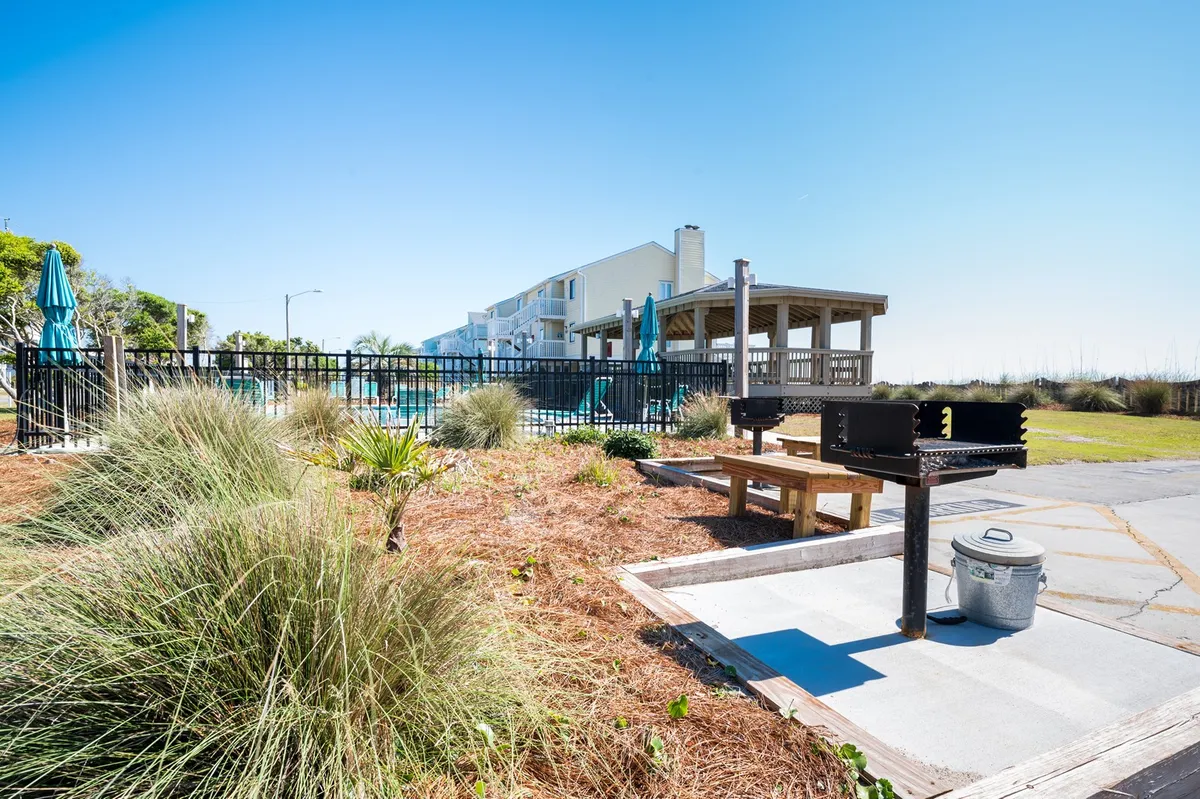 The image features a vibrant outdoor grilling area adjacent to the pool, with landscaped greenery and ample seating for groups. The atmosphere is casual and social, encouraging guests to gather for meals or celebrations.