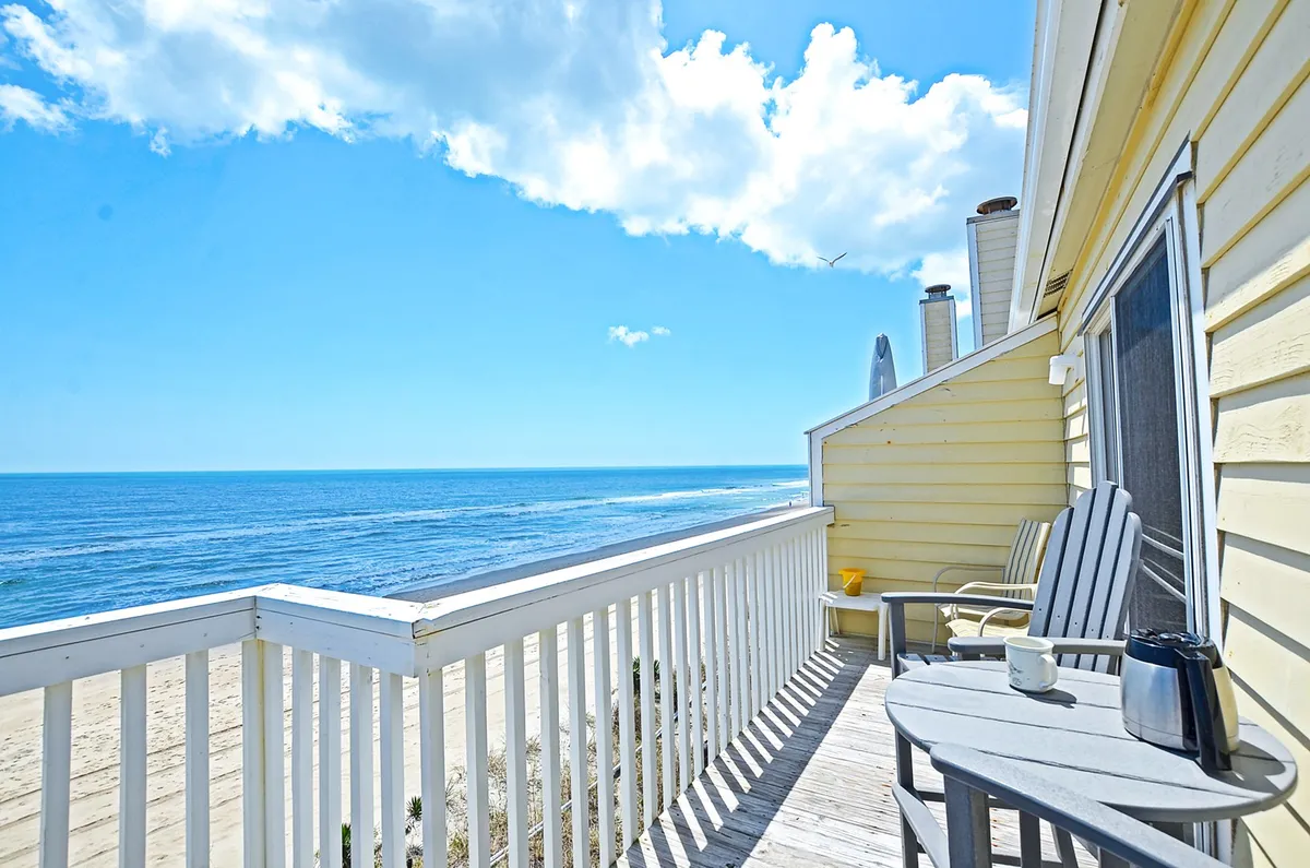 A serene private deck with comfortable deck chairs and a coffee cup set on a small table, overlooking a breathtaking, unobstructed ocean view. The mood is relaxed, suggesting morning coffee or sunset relaxation above the waves.
