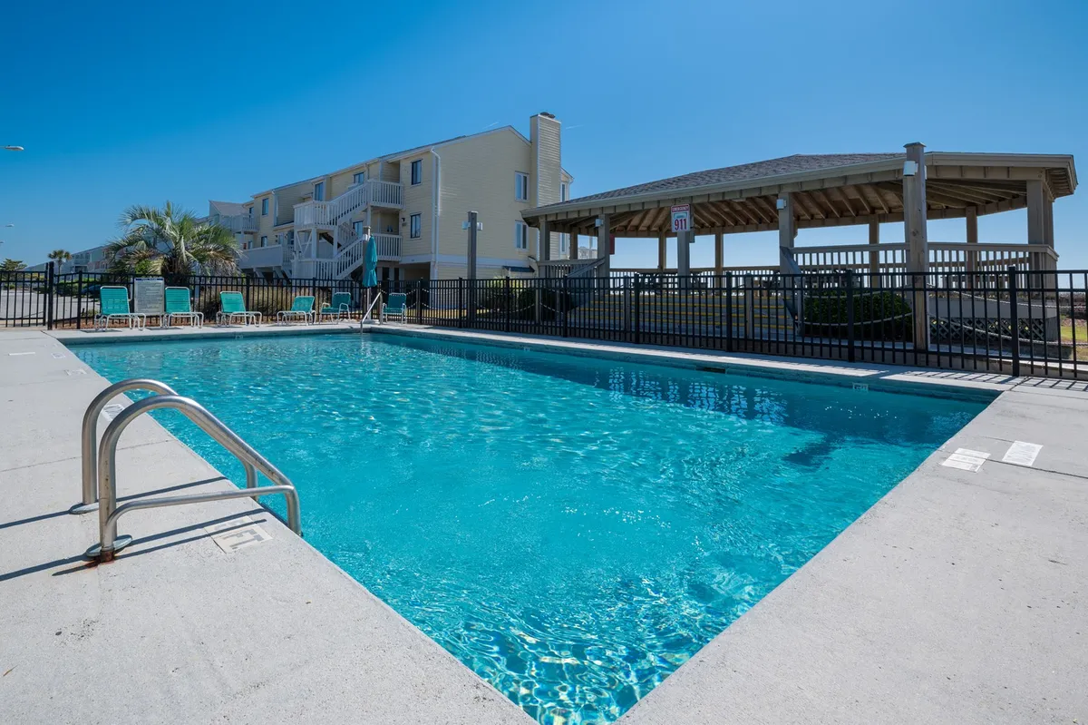 A vibrant outdoor scene featuring a sparkling swimming pool surrounded by lounge chairs, a covered gazebo, and palm trees. The mood is relaxed and social, with ample space for sunbathing, poolside gatherings, and unwinding after a day of exploration.