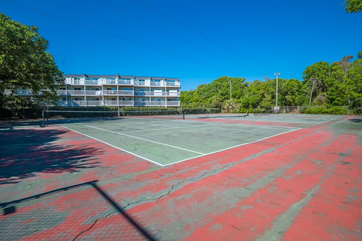 A well-maintained tennis court bordered by lush greenery and a building in the background. The open-air court invites guests to enjoy active matches beneath the sky, adding a dynamic aspect to the array of resort amenities.